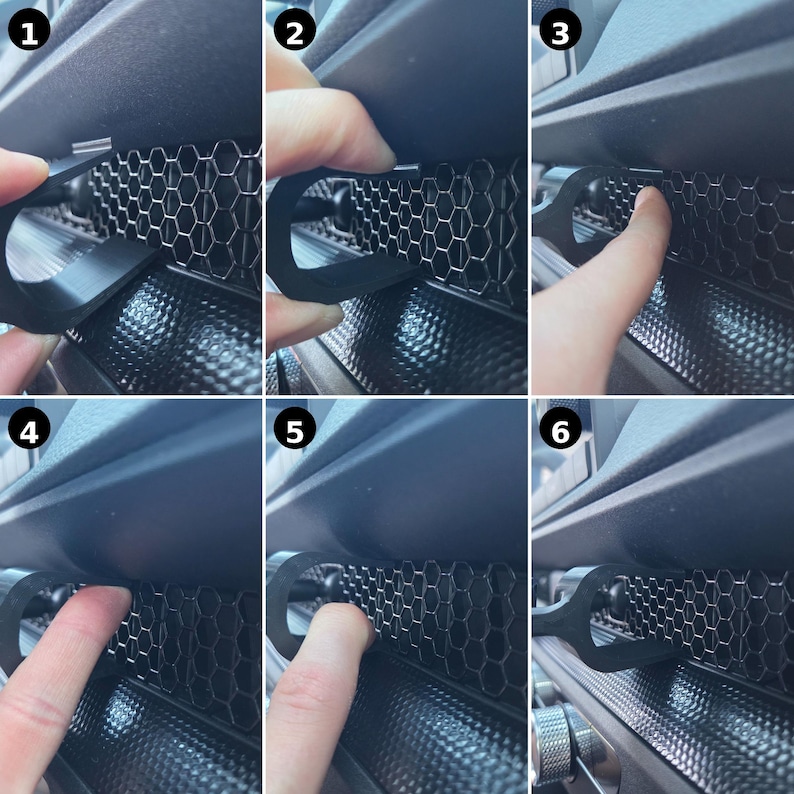 May include: A black, U-shaped plastic clip designed for installation into a vehicle's dashboard air vent. The clip features a curved hook end that inserts into the hexagonal honeycomb grille pattern of the vent, securing it firmly in place.