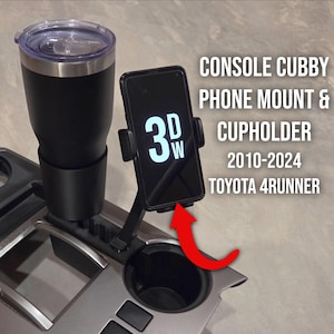 May include: Black console cubby phone mount and cupholder for Toyota 4Runner vehicles. The image shows a black phone mount with a phone displaying "3DW" and a black tumbler in the cupholder. The text on the image reads "CONSOLE CUBBY PHONE MOUNT & CUPHOLDER 2010-2024 TOYOTA 4RUNNER."