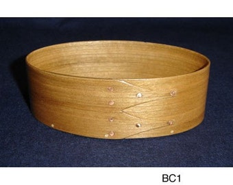 Könnte beinhalten: Eine ovale Holzschale mit hellbrauner Oberfläche. Die Schale hat ein dekoratives Muster aus geflochtenen Streifen und ist mit kleinen Kupfernägeln befestigt.