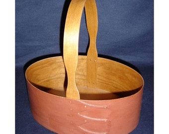 Könnte beinhalten: Ein ovaler Korb aus Holz mit einem braunen Lederboden und einem Holzgriff. Der Korb ist leer.