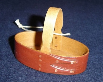 Könnte beinhalten: Ein kleiner Holzkorb mit braunem Lederboden und einem Holzgriff. Der Korb hat ein dekoratives Design auf dem Lederboden und Kupfernieten.