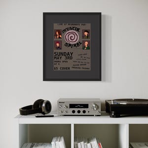 Op de afbeelding: Een ingelijste poster met de tekst "Mystik Spiral" en evenementdetails, waaronder "Zondag 3 mei" en een toegangsprijs van $5. De poster wordt weergegeven boven een plank met een stereoversterker, een koptelefoon en boeken.