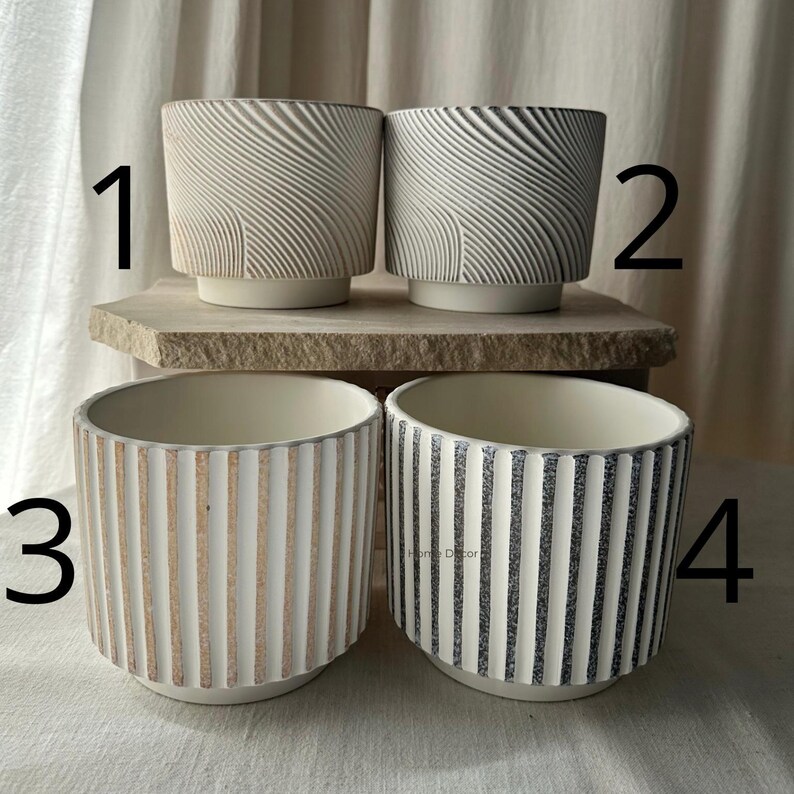 May include: Four ceramic planters in neutral tones. Two have a textured, swirling design, and two feature vertical stripes. The planters are cylindrical with a slightly flared base, suitable for indoor or outdoor use. The planters are ideal for succulents or small plants.