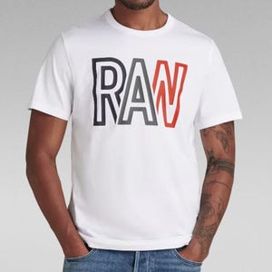 May include: White t-shirt with a black and red "RAW" logo printed on the front.