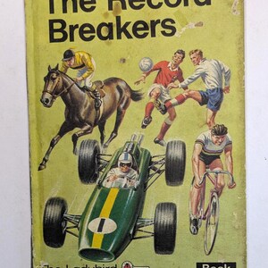 Pode incluir: Capa de livro vintage intitulada "The Record Breakers", com ilustrações de corridas de cavalos, futebol, ciclismo e um carro de corrida. O livro faz parte da série "Ladybird Key Words Easy Readers".