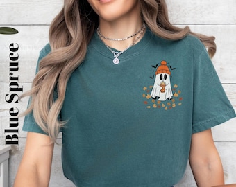 May include: A teal blue t-shirt with a graphic of a ghost wearing a hat and holding a cup of coffee. The ghost is surrounded by autumn leaves.