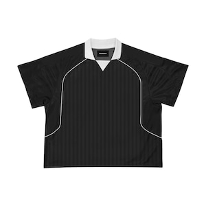 Peut inclure: Maillot de football à manches courtes noir avec des bordures blanches et un col blanc. Le maillot est à rayures et le mot "Goodwear" est imprimé sur le col.