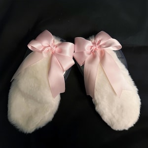 May include: A pair of white fluffy bunny ears with pink satin bows. The bows are tied in a knot at the center and have long tails.