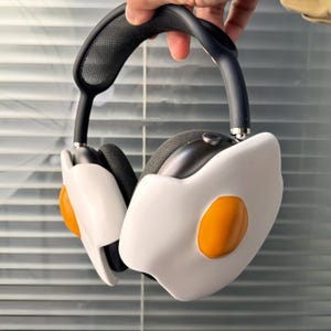 Könnte beinhalten: Schwarze Kopfhörer mit einem weißen und orangefarbenen, eiförmigen Design. Die Kopfhörer haben einen schwarzen Kopfbügel und ein Netzdesign am Kopfbügel.