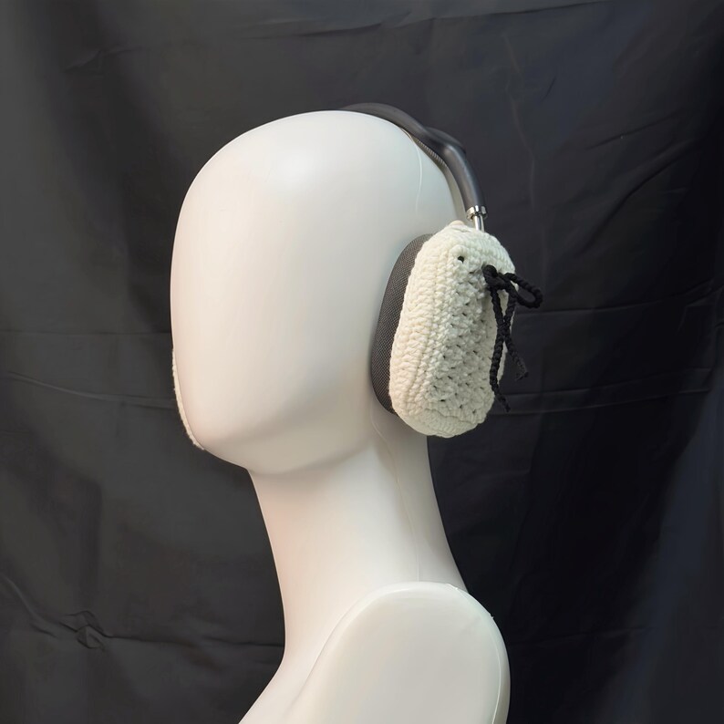 May include: White crocheted ear warmers with black ties attached to the top. The ear warmers are worn on a white mannequin head.