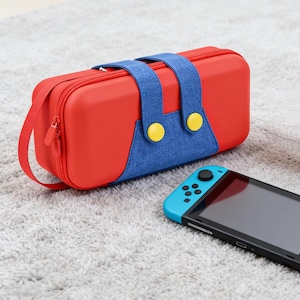 Może przedstawiać: Czerwono-niebieski futerał do przenoszenia Nintendo Switch z żółtymi akcentami w postaci guzików. Futerał ma pasek na ramię i zapięcie na zamek błyskawiczny. Konsola Nintendo Switch znajduje się obok futerału.