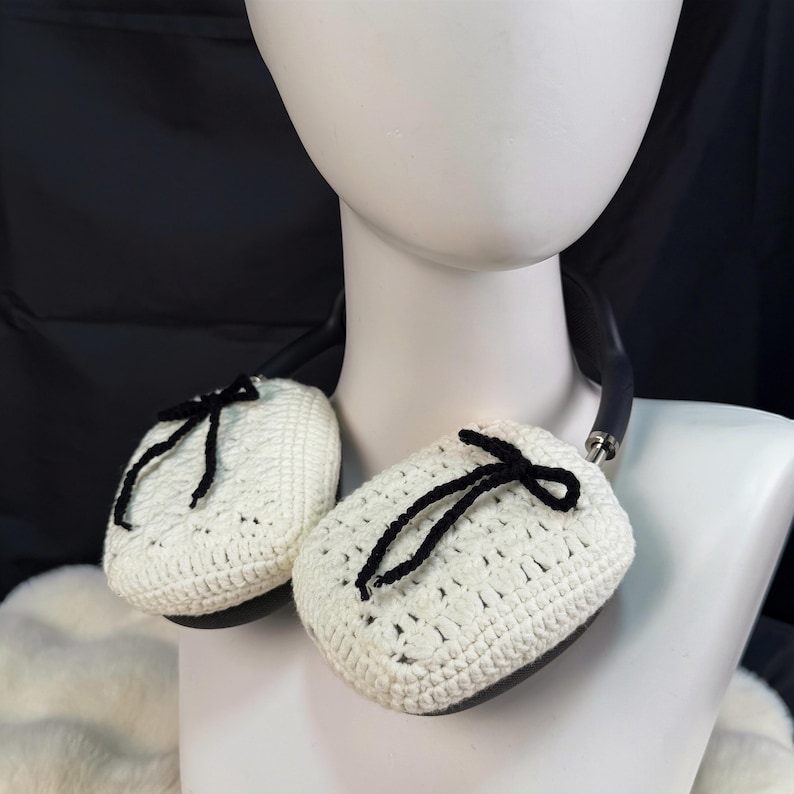 May include: White crocheted earmuffs with black ribbon ties. The earmuffs are attached to a black headband.