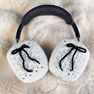 May include: White crocheted earmuffs with black ribbon accents, designed to fit over headphones.