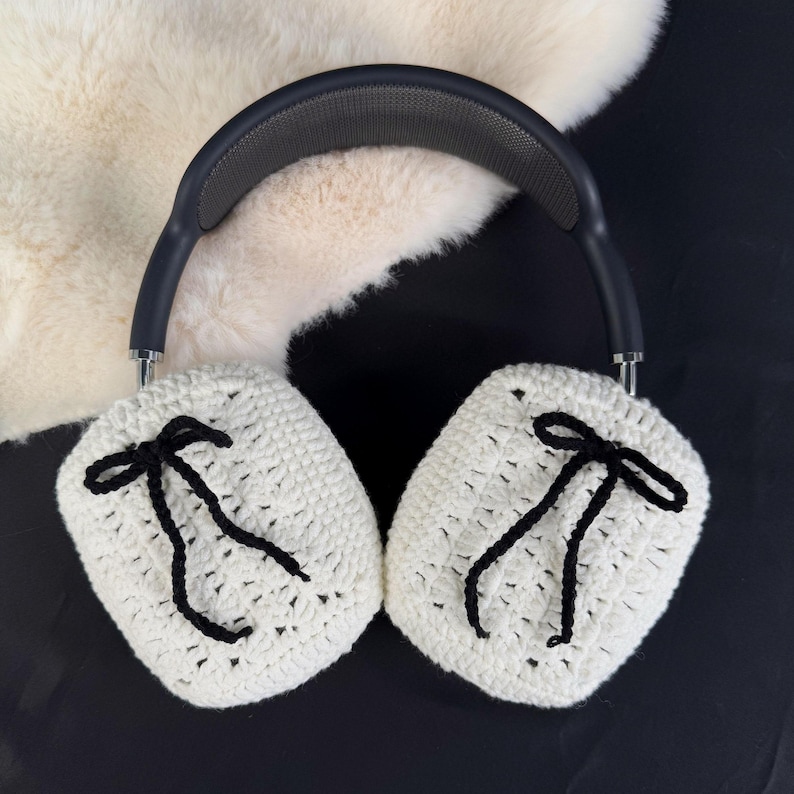 May include: White crocheted earmuffs with black ribbon ties. The earmuffs are attached to a black headband.