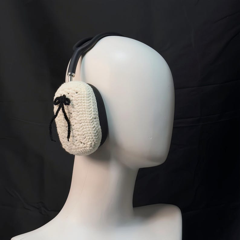 May include: White crocheted earmuffs with black ribbon accents and a black headband. The earmuffs are worn on a white mannequin head.