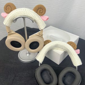 Peut inclure: Deux paires de casques avec des bandeaux en crochet en forme de t&ecirc;te de mouton. Les bandeaux sont blancs avec des oreilles brunes et des nez roses. Les casques sont beige et noirs.