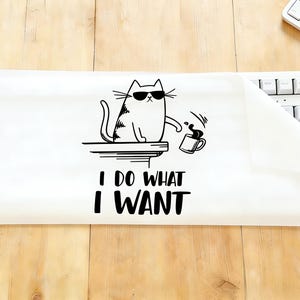 Puede incluir: Funda blanca para teclado con un gráfico de gato en blanco y negro con gafas de sol y una taza de café. El texto "I DO WHAT I WANT" está debajo del gato. La funda está sobre una superficie de madera.