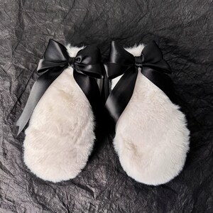 May include: A pair of white fur mittens with black satin bows tied around the wrists.