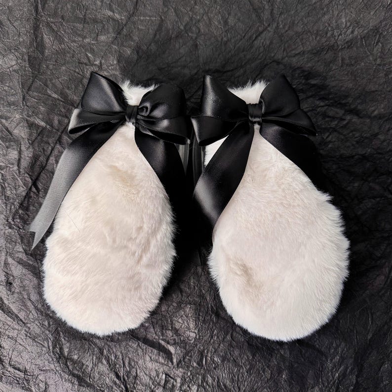 May include: A pair of white fur mittens with black satin bows tied around the wrists.