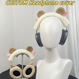 Peut inclure: Une housse de casque blanche en crochet avec des oreilles brunes et roses. La housse est pr&eacute;sent&eacute;e sur un casque noir et un casque beige.