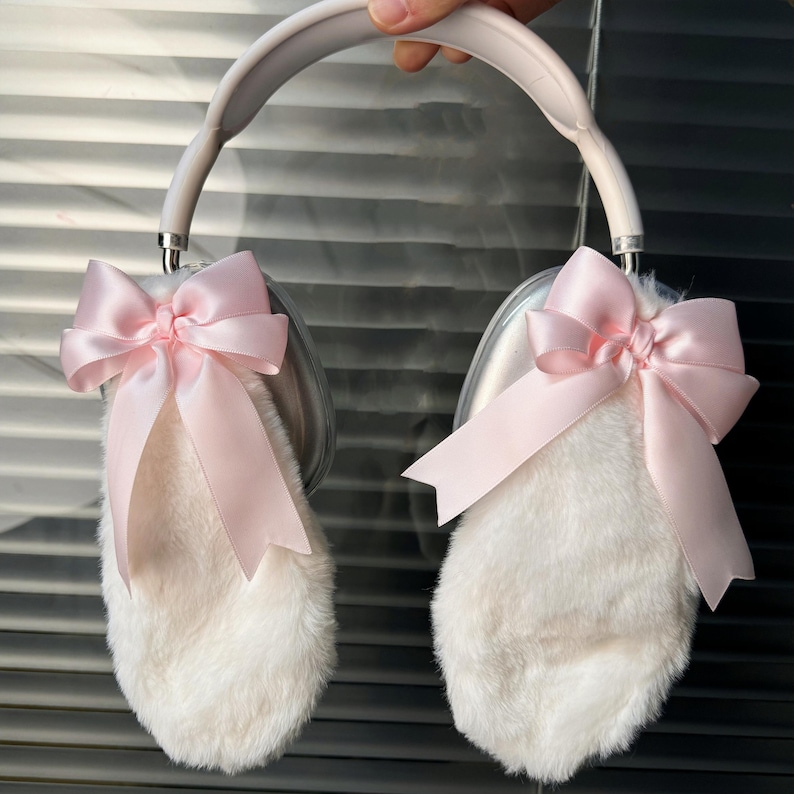 May include: White faux fur headphones with pink satin bows on each earcup. The headband is silver.