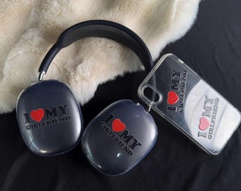 May include: Two black wireless headphones with the text "I love my girlfriend" and a red heart on each earcup. A clear phone case with the same text and heart design is also shown.