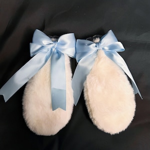 May include: A pair of white fluffy bunny ears with light blue satin bows. The bows are tied in a large knot and have long tails.