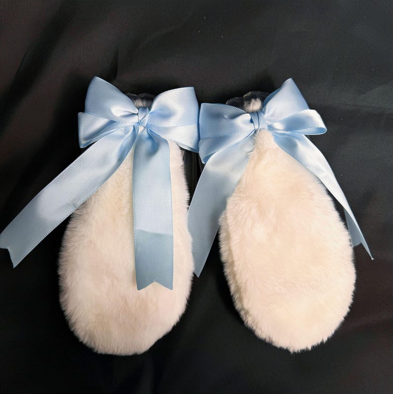 May include: A pair of white fluffy bunny ears with light blue satin bows. The bows are tied in a large knot and have long tails.