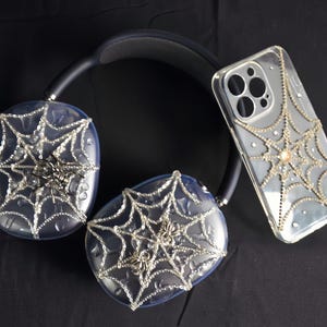 May include: A pair of black headphones with clear earcups decorated with a spiderweb design and rhinestones. A clear phone case with a spiderweb design and rhinestones is also pictured.