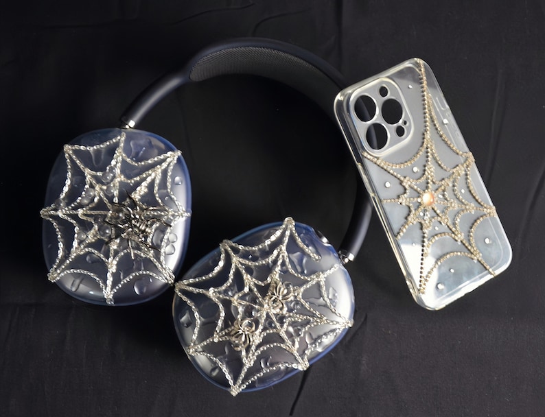 May include: A pair of black headphones with clear earcups decorated with a spiderweb design and rhinestones. A clear phone case with a spiderweb design and rhinestones is also pictured.