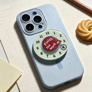 May include: A light blue smartphone case featuring a circular attachment designed like a clock face. The attachment has a pale green background with black numbers 1 through 12 and a red center with the white text Finish the work at.
