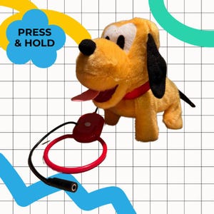 May include: A plush toy of a yellow dog with black ears, a red collar, and a pink tongue sticking out. The toy has a red button and a black cord attached. Text on the image reads "PRESS & HOLD".