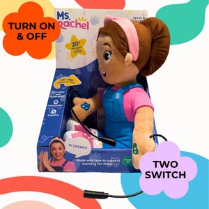 以下が含まれることがあります： 箱に入ったMs. Rachelのぬいぐるみ。人形はピンクのシャツと青いオーバーオールを着ています。箱には「Ms. Rachel」と「20+ Phrases Songs」と書かれています。人形には2つのスイッチがあり、「TURN ON & OFF」と「TWO SWITCH」という文字があります。