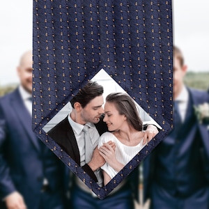 May include: Dark blue tie featuring a diamond pattern and a photograph of a couple. The tie has a navy blue background with a repeating pattern of small gold squares. The photo shows a man and woman.