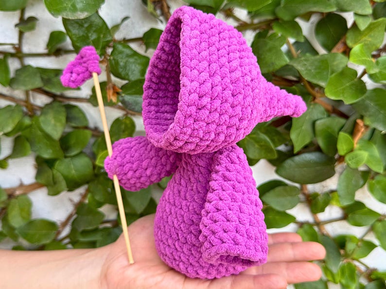 May include: A purple crocheted hooded doll holding a wooden stick with a pink heart-shaped top.