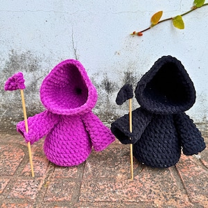 May include: Two crocheted hooded figures, one in pink and one in black, holding wooden sticks with small flags at the top.