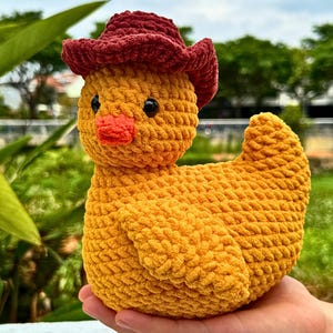 Pu&ograve; includere: Un'anatra all'uncinetto gialla fatta a mano con un cappello da cowboy bordeaux. L'anatra ha un becco arancione brillante e occhi neri. Il peluche &egrave; morbido e strutturato, perfetto per la cameretta di un bambino o come oggetto decorativo.