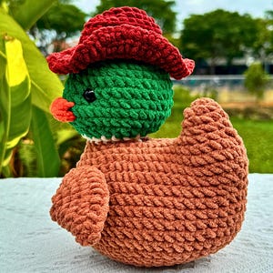 Pu&ograve; includere: Un'anatra all'uncinetto fatta a mano con un cappello rosso, testa verde, becco arancione e corpo marrone. L'anatra &egrave; fatta di filato morbido e ha un aspetto strutturato. &Egrave; un oggetto decorativo stravagante e affascinante.