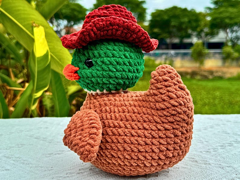 Pu&ograve; includere: Un'anatra all'uncinetto fatta a mano con un cappello rosso, testa verde, becco arancione e corpo marrone. L'anatra &egrave; fatta di filato morbido e ha un aspetto strutturato. &Egrave; un oggetto decorativo stravagante e affascinante.
