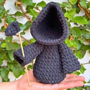 May include: A black crocheted hooded figure with a long stick, resembling a grim reaper, held in a hand.