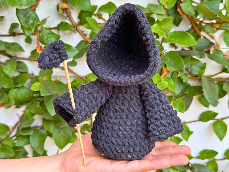 May include: A black crocheted hooded figure with a long stick, resembling a grim reaper, held in a hand.