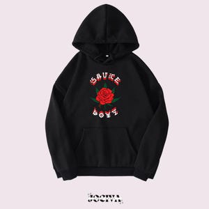 Puede incluir: Sudadera con capucha negra con bolsillo delantero y cord&oacute;n. La parte delantera presenta un gr&aacute;fico de rosa roja con hojas verdes y el texto "SAUCE BOYZ" en rojo y blanco. La sudadera tiene capucha y mangas largas.