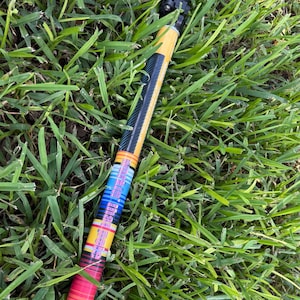 May include: A collapsible trekking pole featuring a black textured handle and a shaft decorated with a vibrant horizontal striped pattern in shades of yellow, orange, red, purple, and blue, with a black carbon fiber-style section near the top.