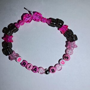 Op de afbeelding: Een handgemaakte armband met roze, zwarte en transparante kralen. De armband bevat stervormige en ronde kralen, met de naam "BRIAR BUSH" gespeld met letterkralen. De armband is geregen op een transparante elastische draad.
