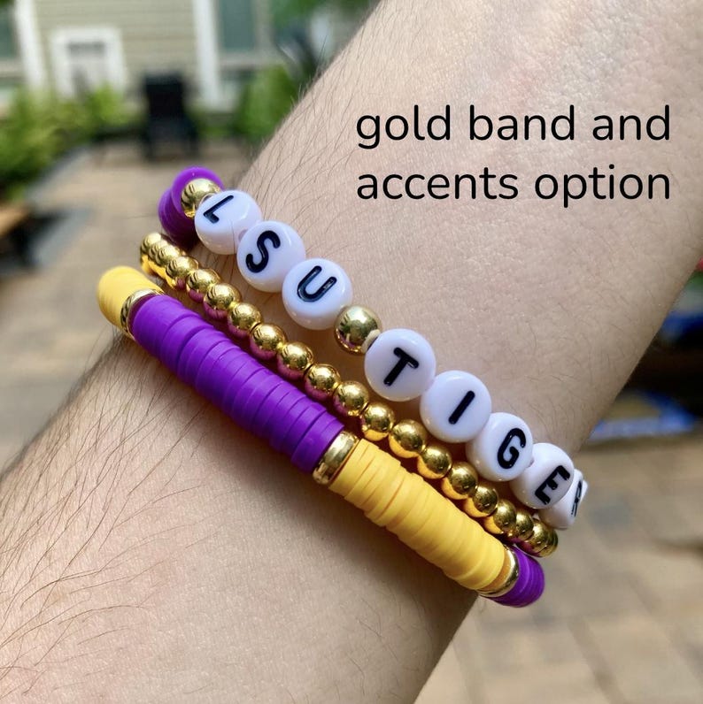 May include: A set of three bracelets with gold beads and purple and yellow bands. The bracelets spell out "LSU TIGERS".