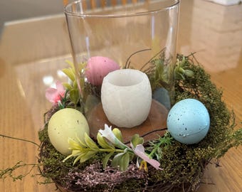 Centrotavola pasquale con nido d'uccello, uova di Pasqua e un portacandele cilindrico in vetro