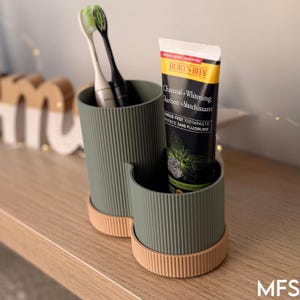 A toothbrush holder with a tube of toothpaste and a toothbrush inside it, placed on a wooden surface.