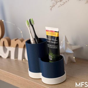 A blue toothbrush holder with a tube of dental floss and a toothbrush placed inside it, sitting on a wooden shelf.