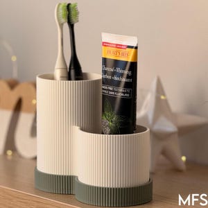 A toothbrush holder with two toothbrushes and a tube of dental floss on a wooden surface.