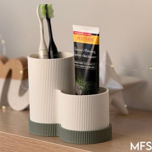 A white toothbrush holder with a tube of toothpaste and a black electric toothbrush inside it, placed on a wooden surface.